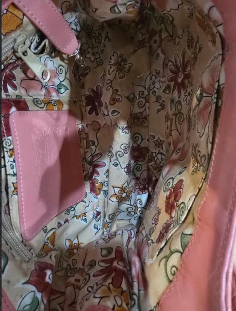 Peut inclure: Sac &agrave; main en cuir rose avec un int&eacute;rieur &agrave; motifs floraux. Le sac est dot&eacute; d'une &eacute;tiquette en cuir rose et d'une fermeture &eacute;clair argent&eacute;e. La doublure int&eacute;rieure est de couleur cr&egrave;me avec un motif de fleurs et de papillons.