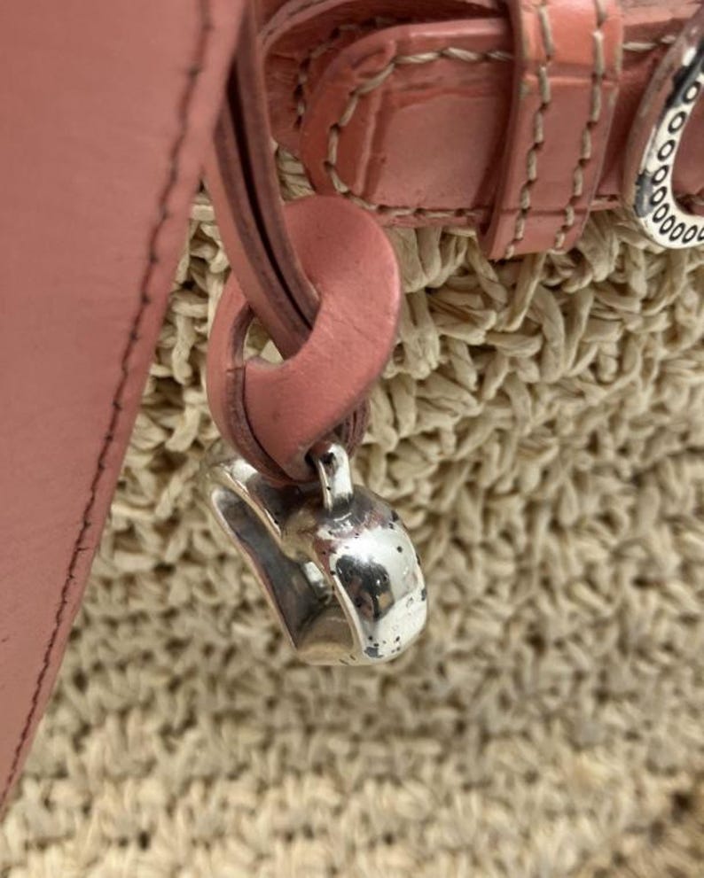 Peut inclure: Gros plan sur un sac &agrave; main en cuir rose avec une base en paille tress&eacute;e. Le sac est orn&eacute; d'un charm argent&eacute; et d'une sangle et d'une boucle en cuir rose. Le design du sac est simple et &eacute;l&eacute;gant.