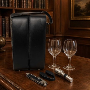 May include: A black leather wine carrier case with a top handle, accompanied by two clear glass wine goblets, a silver-toned metal corkscrew, a black plastic foil cutter, and a cylindrical silver-toned metal wine stopper with a black rubber ring.