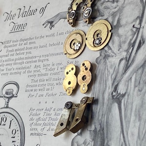 May include: An assortment of vintage watch parts in gold and silver tones, including gears and levers, are arranged on a printed page with the text "The Value of Time" and "Elgin Watches."