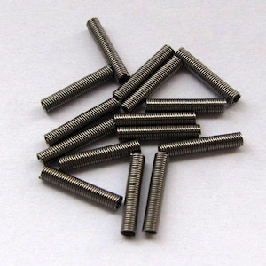 May include: A group of 13 silver metal springs, some are stacked on top of each other, some are laying flat. The springs are all the same size and shape.