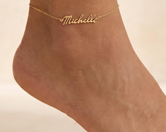 Könnte beinhalten: Ein goldfarbenes Fußkettchen mit einer zarten Kette und einem mittigen Namensanhänger, auf dem der Name Michelle in Schreibschrift eingraviert ist. Das Schmuckstück ist mit einer dünnen, polierten Gliederkette für das Fußgelenk gestaltet.