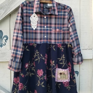 May include: A handmade dress with a plaid top in shades of blue, pink, and beige, and a navy blue floral skirt. The dress features a white lace embellishment and a small embroidered patch with flowers. The collar and pocket are trimmed with pink lace.