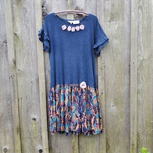 Könnte beinhalten: Ein marineblaues Kleid mit einem Rock mit Blumenmuster. Das Kleid hat einen Rüschenkragen und eine Reihe von rosa Stoffblumen über der Brust.