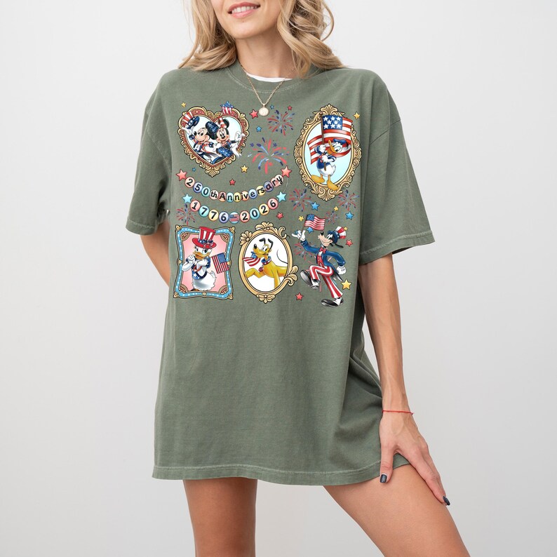 Pode incluir: Camiseta verde-oliva com personagens patri&oacute;ticos da Disney em molduras ornamentadas. A camisa inclui Mickey e Minnie Mouse, Pato Donald, Pateta e Pluto, com o texto "250th Anniversary 1776-2026."
