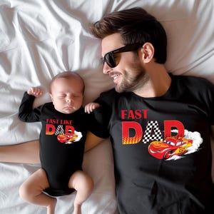 Pode incluir: Camisetas pretas e um body de beb&ecirc; com tema de carro de corrida. A camisa do adulto diz "Fast Dad" com uma bandeira quadriculada e um carro de corrida vermelho. O body do beb&ecirc; diz "Fast Like Dad".