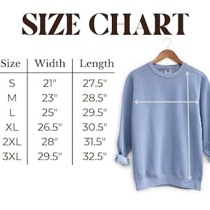 May include: A light blue sweatshirt hangs on a wooden hanger, with a size chart displayed to the left. The chart lists sizes S to 3XL, with corresponding width and length measurements in inches. The text "SIZE CHART" is at the top.