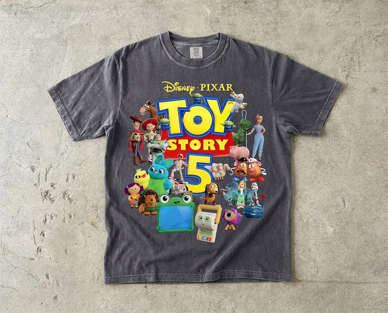 May include: A charcoal gray short-sleeve t-shirt featuring a graphic print of various Toy Story characters surrounding the large yellow text Toy Story 5 and the Disney Pixar logo at the top. The shirt has a crew neckline and a vintage-style wash.