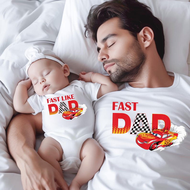 Pode incluir: Um body branco com o texto "FAST LIKE DAD" e um desenho de carro de corrida, ao lado de uma camiseta branca com "FAST DAD" e um desenho de carro a condizer. O beb&eacute; e o adulto est&atilde;o deitados numa cama branca.