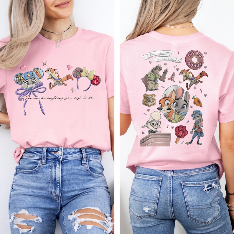 May include: A light pink t-shirt featuring Zootopia character graphics. The front displays Judy Hopps, Nick Wilde, and a donut headband with the text "You can be anything you wish to be." The back shows a collage of characters and icons.