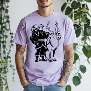 May include: A light purple t-shirt featuring a black graphic of a character from the animated film "Frozen" with a reindeer. The character is holding a pickaxe and a bag. The reindeer has a harness.