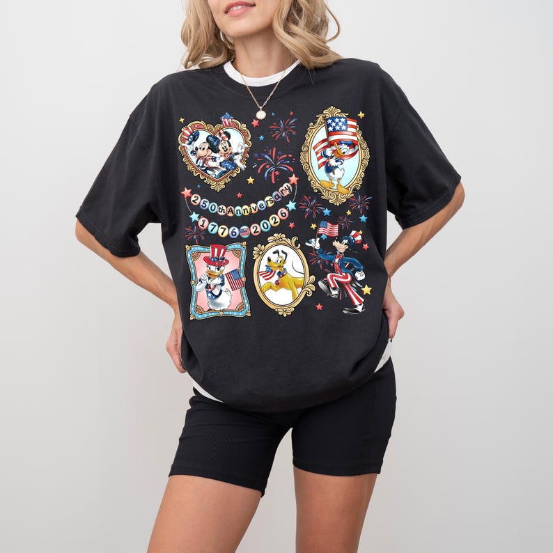 Pode incluir: Camiseta preta com personagens patri&oacute;ticos da Disney em molduras ornamentadas. Mickey e Minnie Mouse, Pato Donald, Pateta e Pluto s&atilde;o retratados com bandeiras americanas e desenhos de fogos de artif&iacute;cio. A camiseta tamb&eacute;m inclui o texto "250th Anniversary 1776-2026".