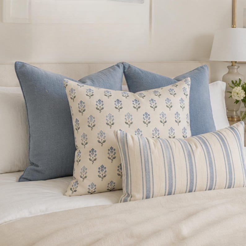 May include: A collection of decorative throw pillows featuring two solid blue square pillows, one cream square pillow with a repeating blue floral pattern, and one rectangular lumbar pillow with vertical blue and cream stripes.