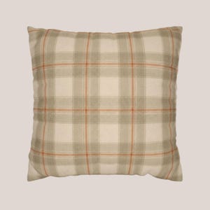 May include: A square throw pillow featuring a plaid pattern in shades of cream, light gray, and thin orange lines. The fabric has a visible woven texture, and the design consists of intersecting horizontal and vertical stripes forming a grid.