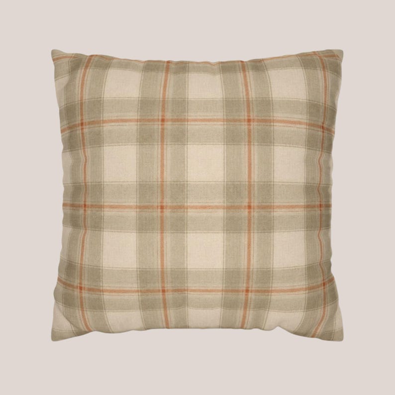 May include: A square throw pillow featuring a plaid pattern in shades of cream, light gray, and thin orange lines. The fabric has a visible woven texture, and the design consists of intersecting horizontal and vertical stripes forming a grid.