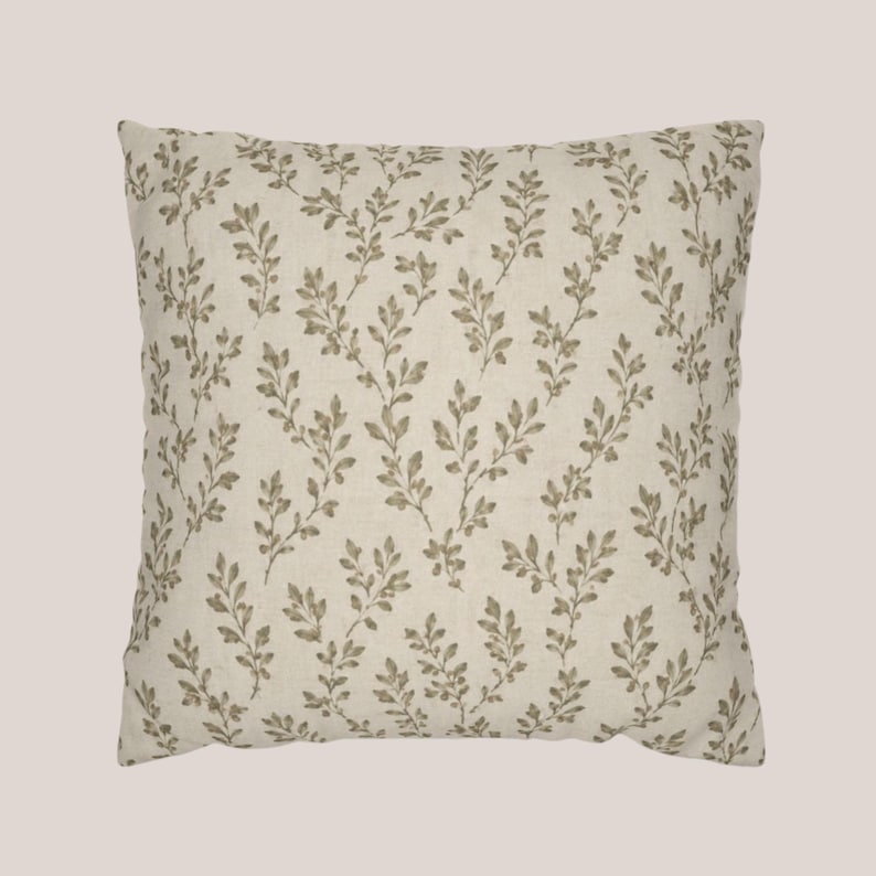May include: A square throw pillow featuring an off-white or cream-colored fabric base. The surface is decorated with a repeating pattern of small, delicate olive-green leafy vine sprigs arranged in a vertical, branching orientation across the cover.