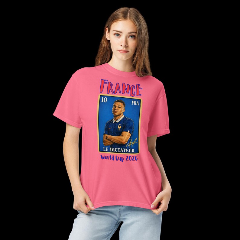 May include: A pink t-shirt featuring a graphic of a soccer player in a blue and gold design. The design includes the word "France", the number "10", and the text "World Cup 2026".