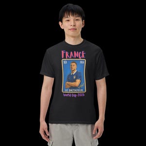 May include: Black t-shirt featuring a graphic of a soccer player in a blue jersey, with the word "FRANCE" above. The graphic includes the text "LE DICTATEUR World Cup 2026".
