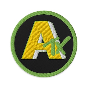 May include: Embroidered patch with a yellow "A" and green "TX" letters on a black background, framed by a green border. The patch is circular in shape and suitable for clothing or accessories.