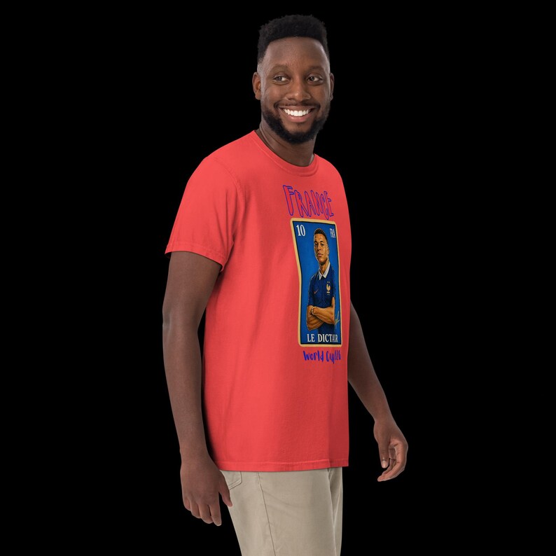 May include: A red t-shirt featuring a blue and white graphic of a soccer player in a blue jersey. The graphic includes the word "FRANCE" and the text "LE DICTEUR world cup".