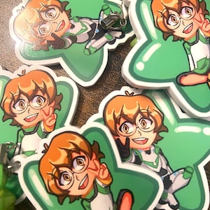 May include: Several green star-shaped charms with cartoon illustrations of a character with orange hair, glasses, and a green and white outfit. The character is making a peace sign or lying down. The charms have a white border and a metal clasp.