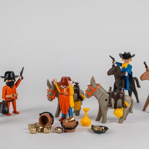 Puede incluir: Un conjunto de figuras de vaqueros de juguete y accesorios. El conjunto incluye figuras a caballo y burros, armados con pistolas. También hay cofres del tesoro, lingotes de oro y otros accesorios, creando una escena del Salvaje Oeste.