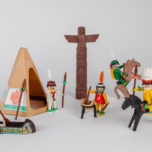 May include: A collection of Native American-themed toy figures and accessories. Includes a brown teepee, a canoe, a totem pole, toy horses, and several figures dressed in traditional attire. The figures are in various poses, some riding horses and others standing.