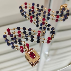 May include: A multi-strand necklace with alternating ruby and sapphire beads, linked by fine gold chains. The necklace has a rectangular pendant with a central ruby gemstone. The necklace reflects light.