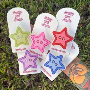 May include: Five star-shaped phone grips in lime green, pink, red, purple, and blue, each featuring two central holes and mounted on white backing cards printed with the text Swirly Owl Studio and the handle @swirlyowlstudio.