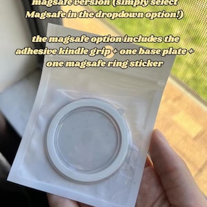 May include: A white and clear Kindle grip in a clear plastic package. The text on the package says the MagSafe option includes an adhesive Kindle grip, a base plate, and a ring sticker.