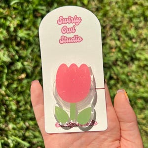 May include: A pink tulip-shaped acrylic phone grip with green leaves and a stem, mounted on a white display card featuring the text Swirly Owl Studio in pink lettering. The tulip design has a subtle glitter finish and a clear acrylic base.