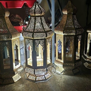 Puede incluir: Varias linternas de metal dorado ornamentadas, con intrincados patrones calados. Las linternas tienen forma hexagonal y están iluminadas desde dentro, proyectando un brillo cálido. Adecuadas para la decoración del hogar.