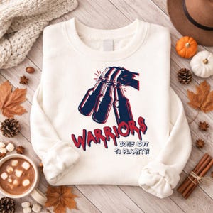 May include: White sweatshirt with a graphic of a hand holding three dark blue bottles with red accents. The word "WARRIORS" is in red, with the phrase "COME OUT TO PLAAYY!" below.