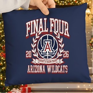 Op de afbeelding: Marineblauw vierkant kussen met de tekst "FINAL FOUR" in wit en rood, samen met "20 26" en "ARIZONA WILDCATS". Het kussen toont een logo van de Universiteit van Arizona en een banner met de tekst "UNIVERSITY OF ARIZONA STADIUM".