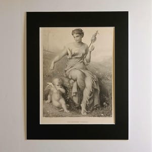 Op de afbeelding: Zwart-wit prent van een klassieke scène met een zittende vrouw die een spil vasthoudt en een kleine cherubijn. De prent is ingelijst in een zwart passe-partout.
