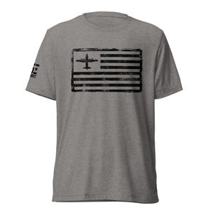 May include: A heather gray t-shirt featuring a distressed black graphic of an airplane within a flag design. The flag has horizontal stripes and a square with the airplane. The left sleeve has the text "AIRTS".