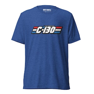 Puede incluir: Camiseta azul de manga corta con el texto "C-130" en blanco, rojo y azul. La camiseta también tiene el texto "A REAL AMERICAN HERO" encima del texto "C-130". La camiseta está hecha de un material suave.
