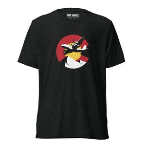 Pode incluir: Uma t-shirt de manga curta em cinzento escuro mesclado com um gráfico da silhueta preta de um avião a voar sobre um sol amarelo e picos de montanha brancos, num fundo circular vermelho. A etiqueta interior do pescoço exibe o texto HERC SHIRTS.