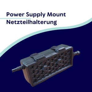 May include: A black power supply mount with a honeycomb design and two velcro straps. The text "Power Supply Mount" and "Netzteilhalterung" are displayed in white on a white and teal background.