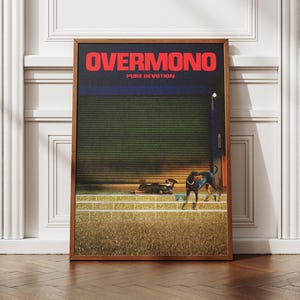 May include: A rectangular framed poster featuring the text OVERMONO and PURE DEVOTION in red letters at the top. The artwork depicts a dark green shuttered building at night with a black dog standing on a grassy field in the foreground.