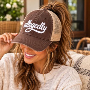 May include: A brown baseball cap with a mesh back and the word allegedly written in white script across the front. The cap features a distressed finish on the brim and front panels, with a structured crown and an adjustable strap at the back.