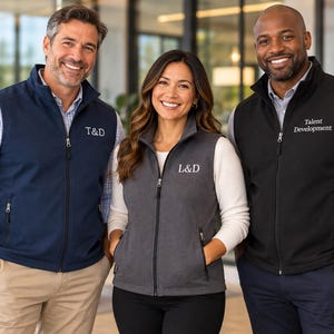 May include: Three sleeveless vests with full-length front zippers and stand-up collars. The left vest is navy blue with T&D embroidered, the center is charcoal gray with L&D, and the right is black with Talent Development embroidered on the chest.