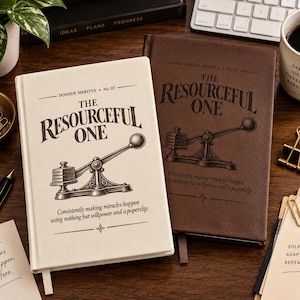 May include: Two hardcover journals, one cream and one dark brown, each featuring the text "Dossier Meritus No. 07", "The Resourceful One", and "Consistently making miracles happen using nothing but willpower and a paperclip" with a vintage press illustration.