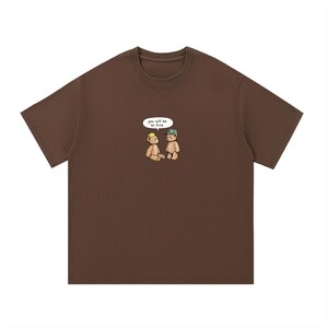May include: A brown t-shirt featuring a cartoon illustration of two teddy bears. One bear wears a crown, the other a cap. A speech bubble above them reads "you will be so fine."