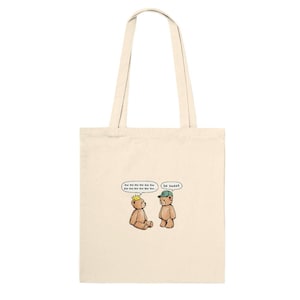 May include: Cream-colored tote bag featuring a cartoon illustration of two teddy bears. One bear wears a crown and the other a cap. Speech bubbles above the bears read "be sweet" and other text.