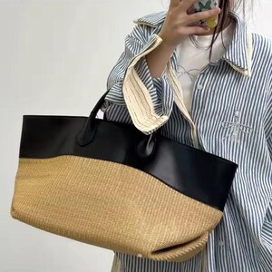 May include: A large tote bag with a woven straw bottom and a black leather top. The bag has two black handles and a spacious interior, perfect for carrying essentials. The bag's design is both stylish and functional.