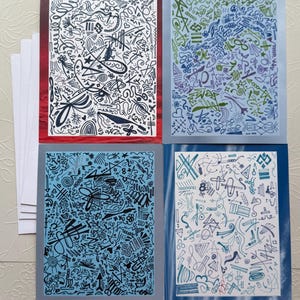 Peut inclure: Quatre cartes de vœux avec des gribouillis abstraits noirs et blancs sur des fonds colorés. Les cartes ont des bordures rouges, bleues et vertes. Une pile de cartes blanches vierges est visible à gauche.