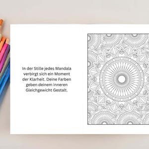 May include: Open book with a black and white mandala design on the right page. The left page has German text. Colored pencils are visible on the top and bottom of the image.
