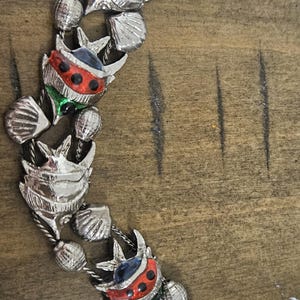 May include: Silver-toned bracelet featuring alternating seashell and ladybug designs. The ladybugs have red, green, and blue accents with black spots. The bracelet is on a wooden surface.