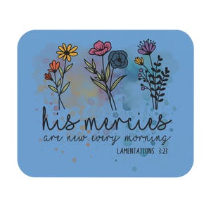 May include: A rectangular light blue sign featuring three hand-drawn floral illustrations in yellow, orange, pink, blue, and purple. Below the flowers, black cursive text reads "his mercies are new every morning" with "LAMENTATIONS 3:23" underneath.
